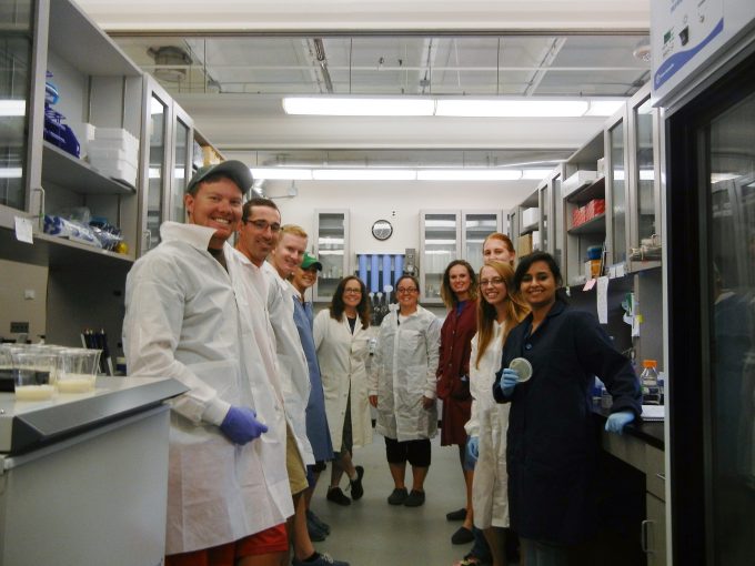 10 researchers in lab coats look at the camera smiling in lab