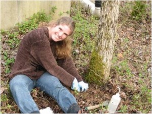 Dr. de Graaff posing for photo while digging next to tree trunk