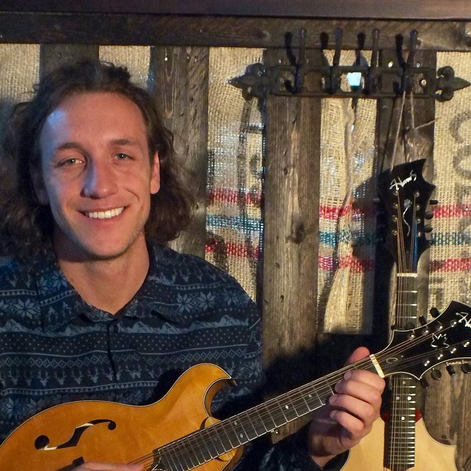 Dillon Haw smiles and strums upon a stringed instrument.