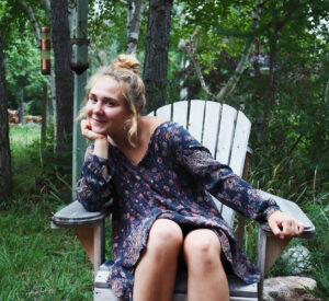 Abbey sitting in a wooden chair in her Saskatchewan garden.