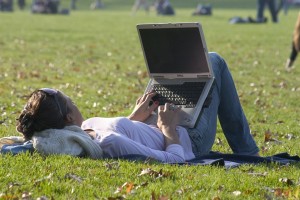 student lying on the grass with a laptop propped on their legs