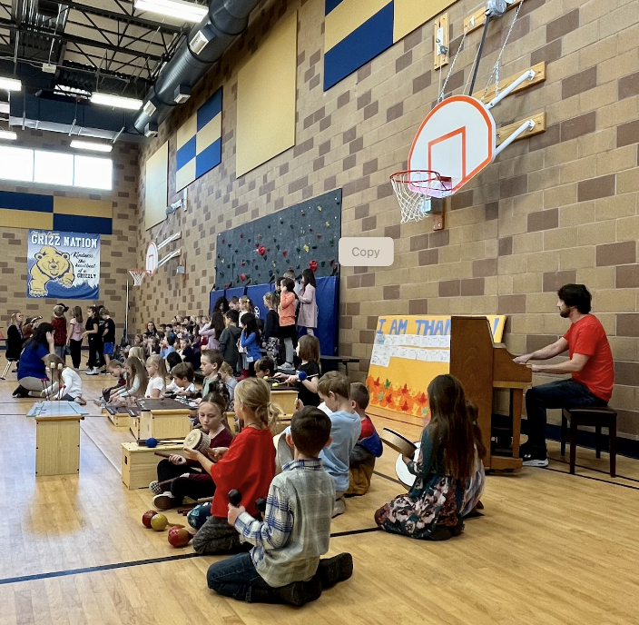 elementary students play with musical instruments in a gym