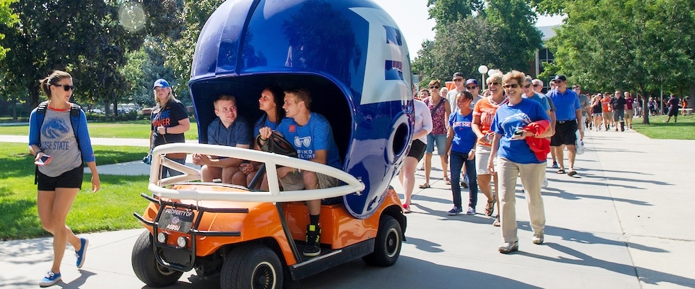 A group of students march behind a Boise State golf cart