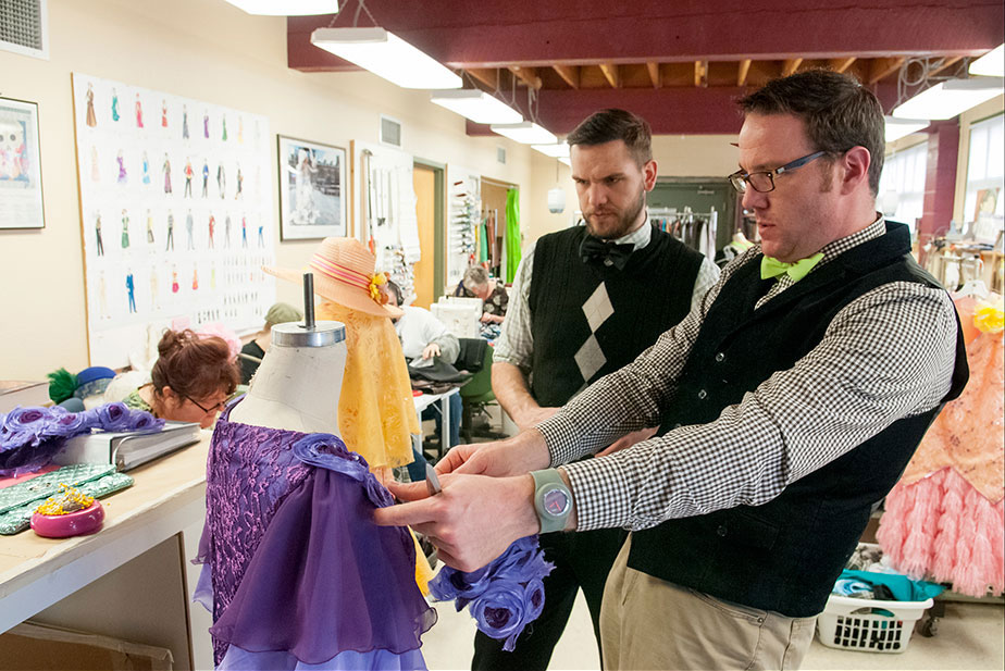Two men adjust garment in theatre dressing room