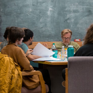 Creative writing students are gathered around a table during a class.