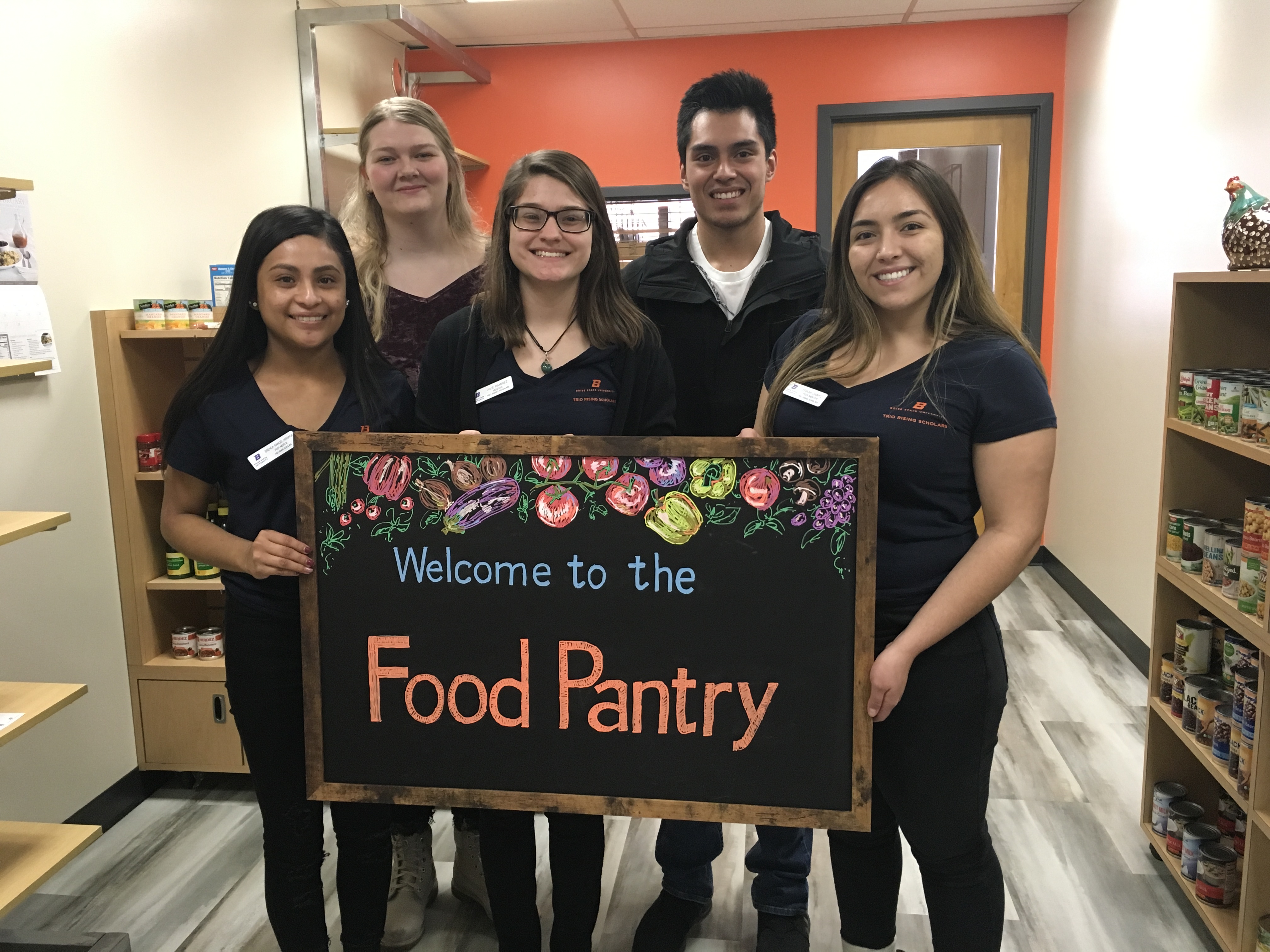 5 Students holding up a "welcome to the food pantry" sign