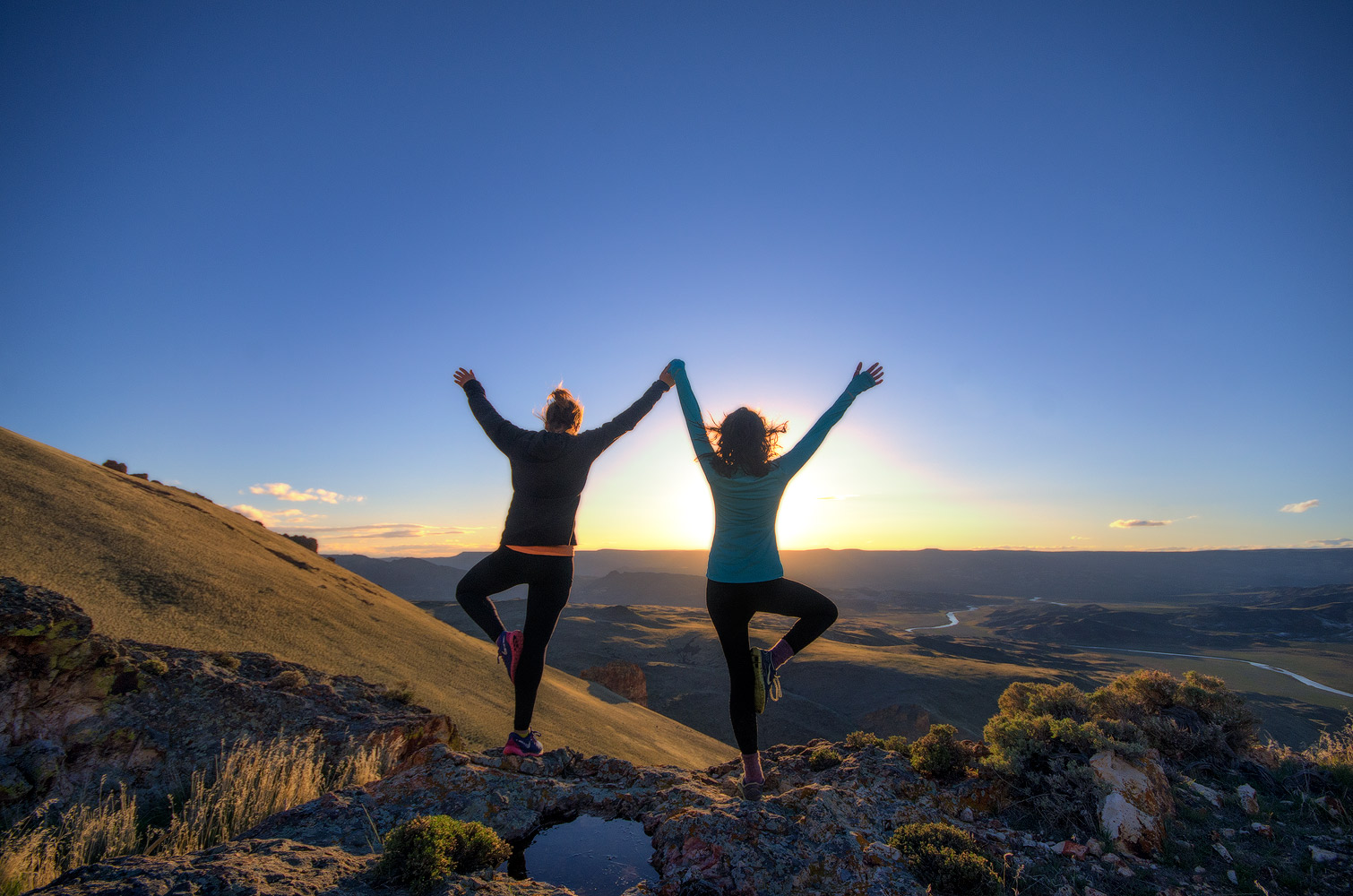Two people stand in mountain pose on a hilltop at sunrise