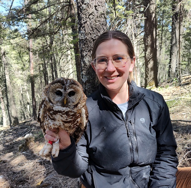 Gustafson smiling and holding a spotted owl in the forest