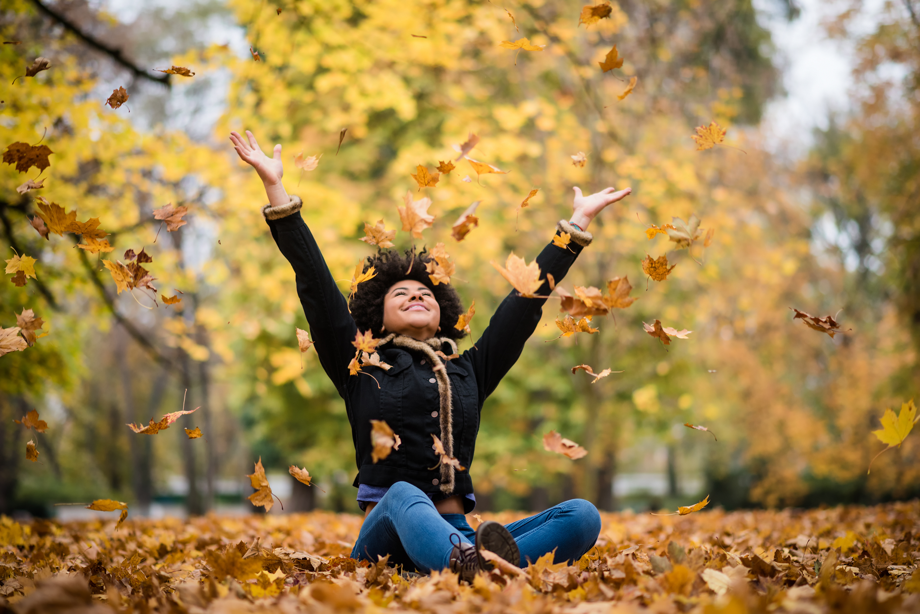 Student sitting in fall leaves and throwing leaves in the air