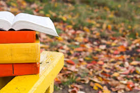 books on an outside table with fallen autumn leaves on the ground