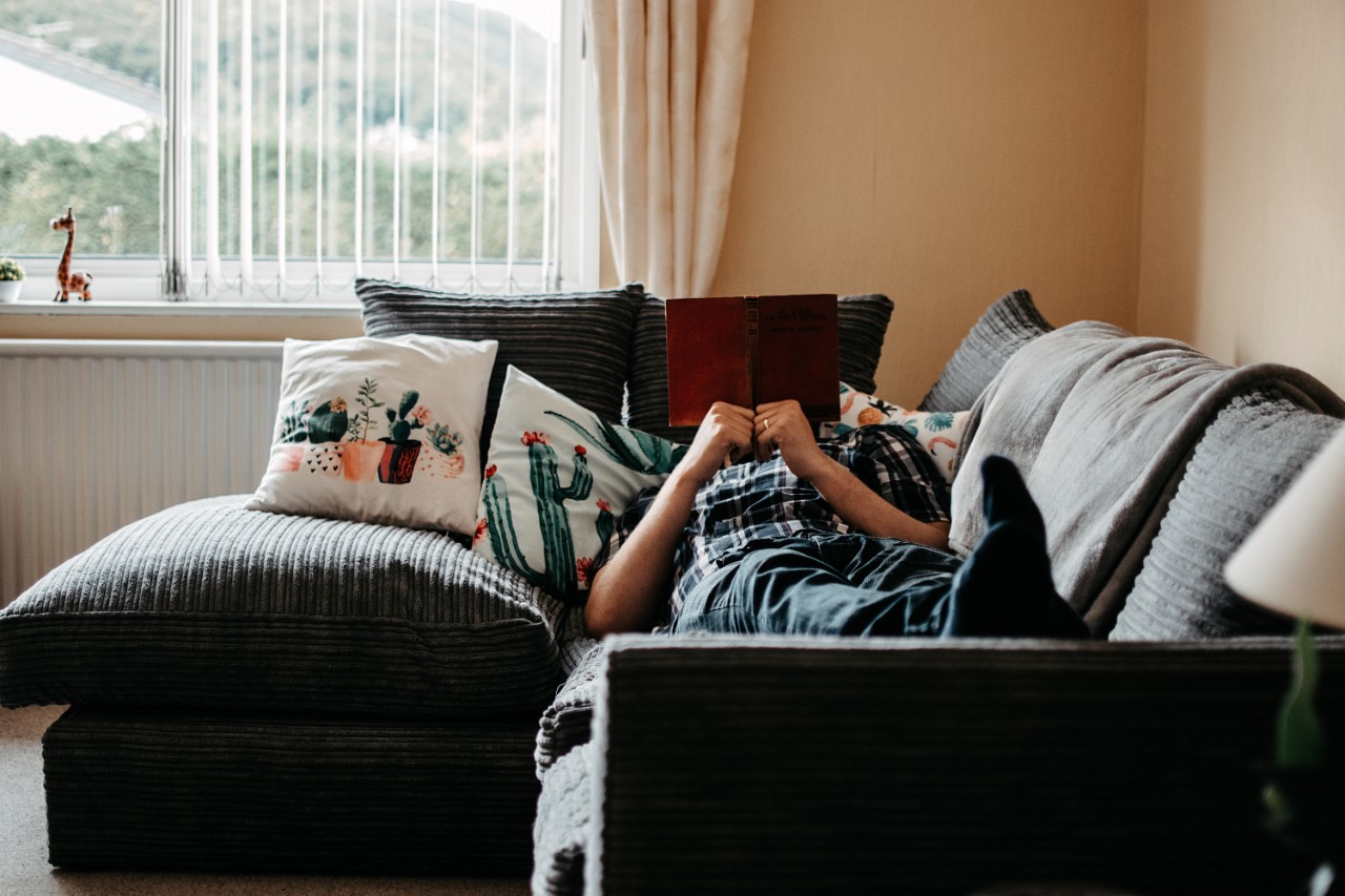 person in shirt and jeans laying on couch with book