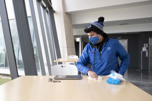 Student wearing a facemask and cleaning a desk