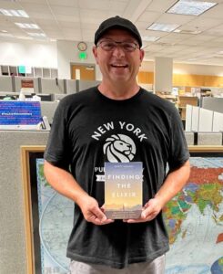 photo of Scott Looney holding his recently published book, Finding the Elixir