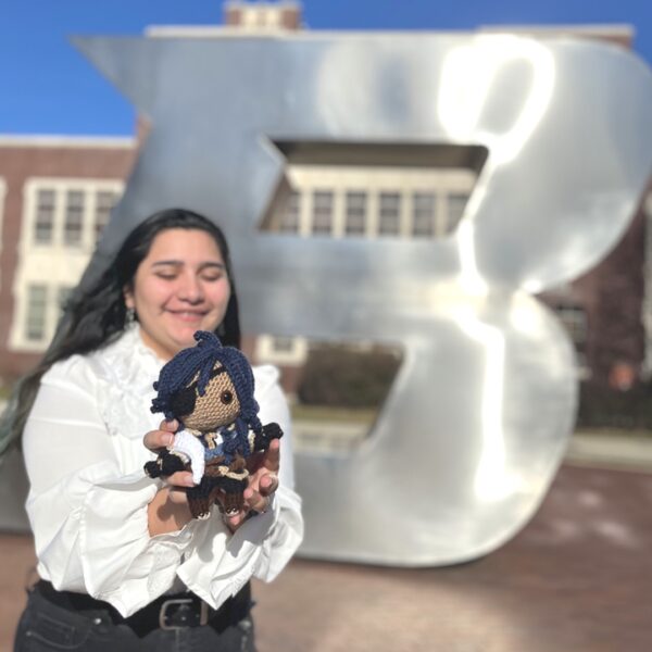 photo of Jasmine Reyes in front of the giant B at university plaza, holding a crocheted character.