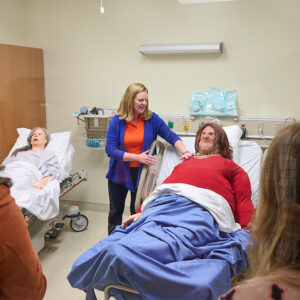 An instructor stands in a simulation room with two practice manikins. 