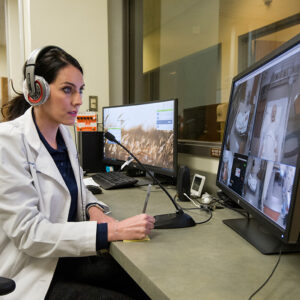 An instructor wearing headphones watches a simulation from the control room
