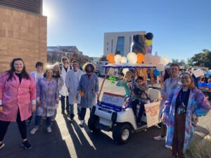 Photo of the Chemistry Club members wearing lab coats and standing next to their parade float made with balloons on a golf cart.