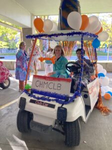 Phot of two Chemistry Club members sitting in the Homecoming parade float golf cart they decorated with balloons and streamers.