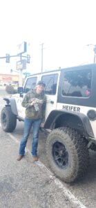 Photo of Kim Cirelli standing next to a white Jeep and holding a cup with black and white cow print