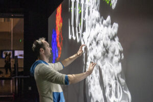 Photo of Konrad Meister manipulating a 3D rendered image of a compound on the interactive touchscreens in the Luminary at Boise State