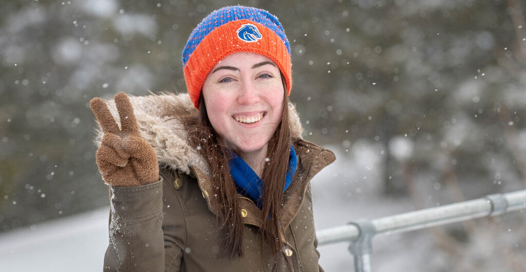 Student standing in the snow, photo showcases shallow depth of field and captures the vibrancy of the falling snow