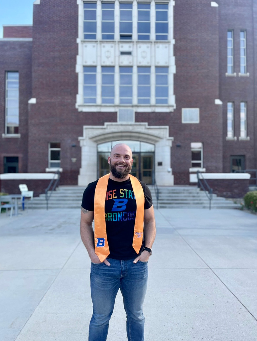 Chris Hughes wears his apricot nursing stole and stands in front of a building on campus.