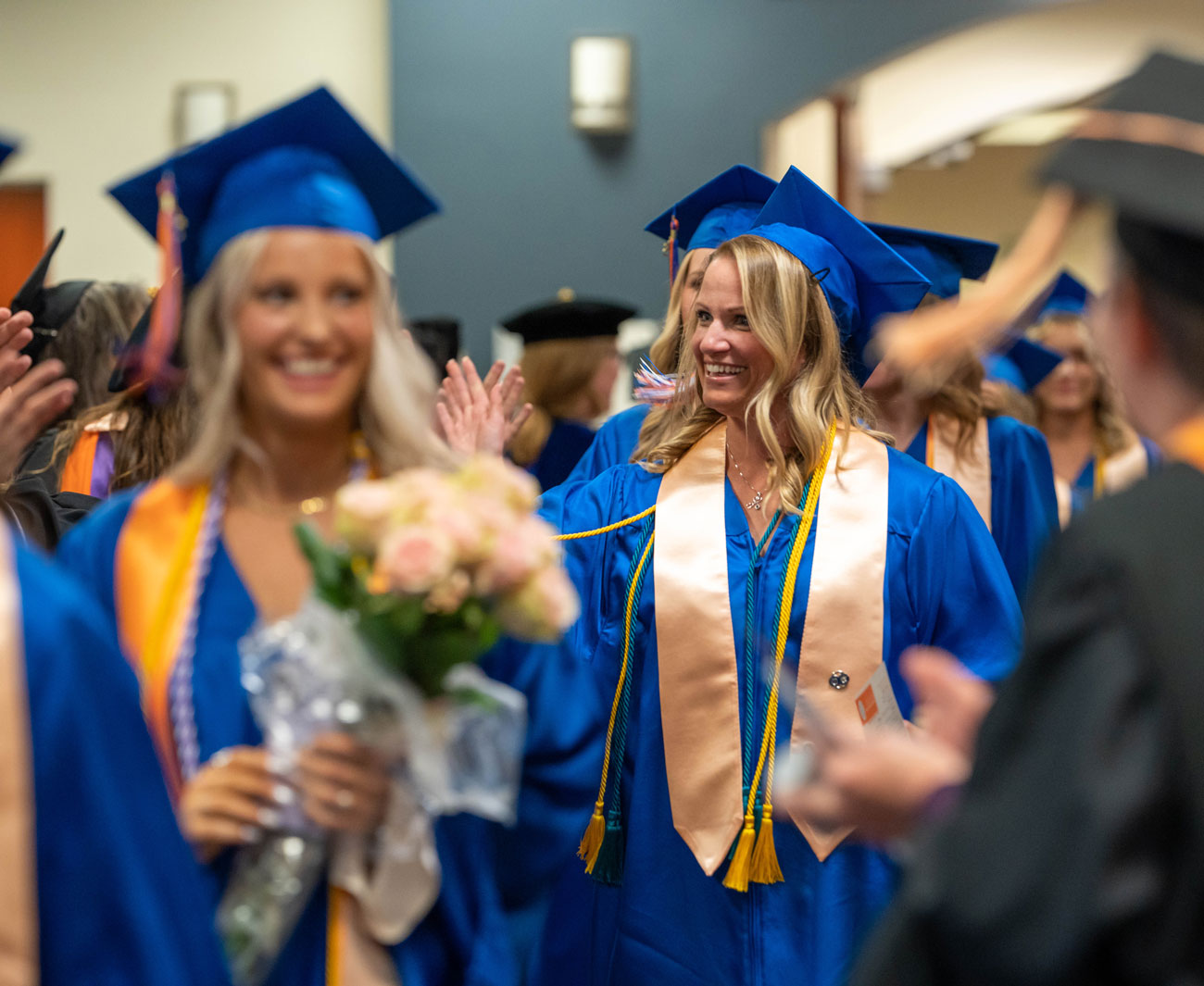 Brynn Sorensen waves to family as the students process during the Convocation ceremony in their regalia.
