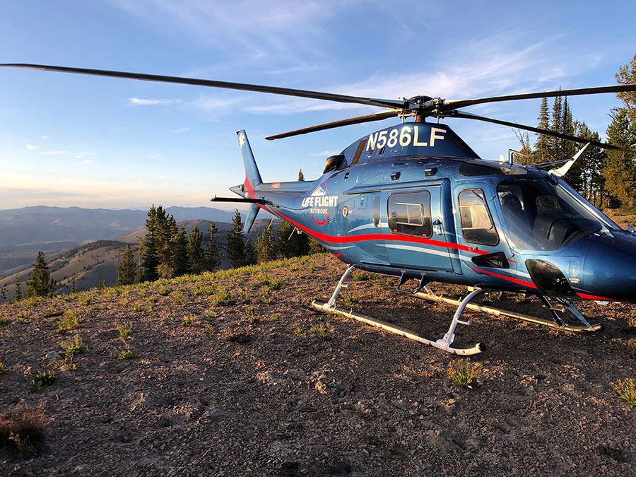 Life Flight helicopter sits on a bluff overlooking mountains and evergreen trees.
