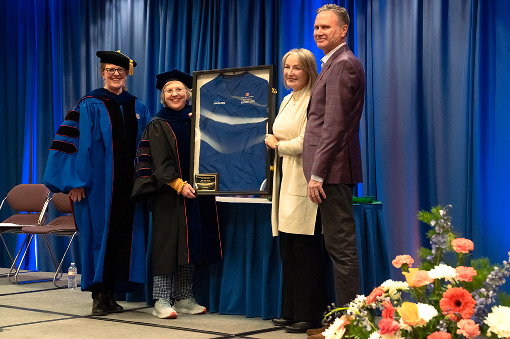 Two nursing professors present a blue scrub in a frame to a donor couple.