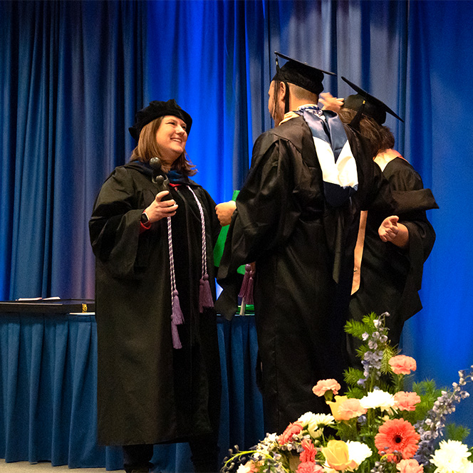 Edy Zepeda is congratulated on stage in his regalia by two other nursing professors.