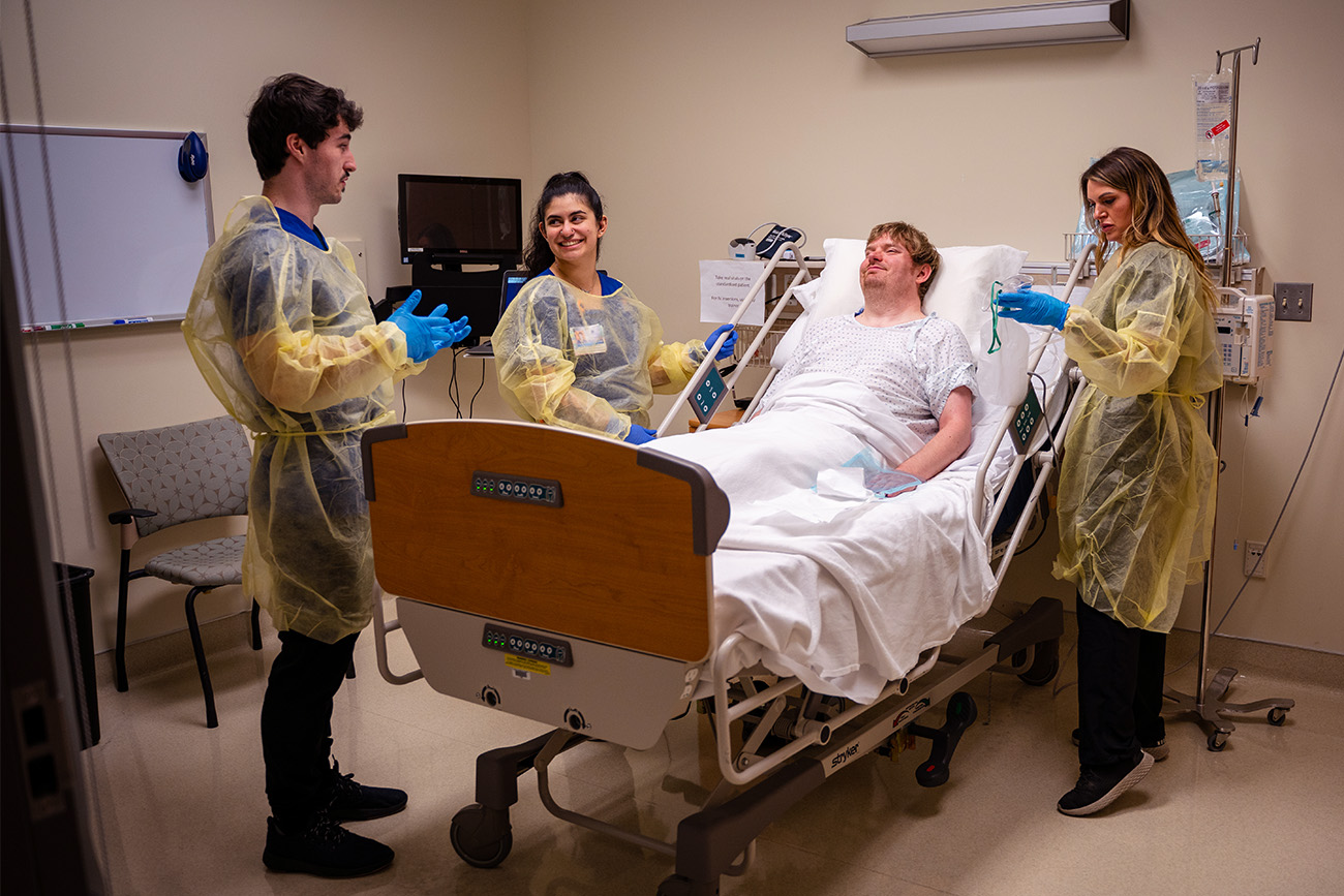 Three nurses wearing PPE tend to a patient lying in a hospital bed.