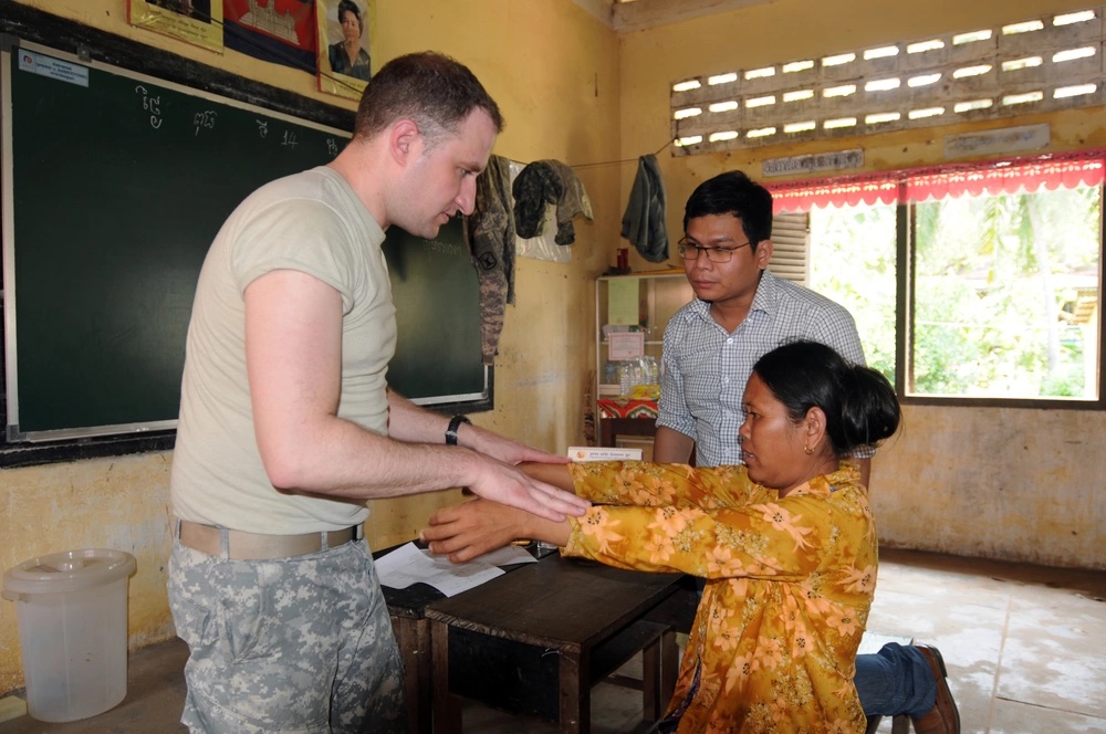 Seckel wears his National Guard uniform and works with a patient in a Cambodian classroom.