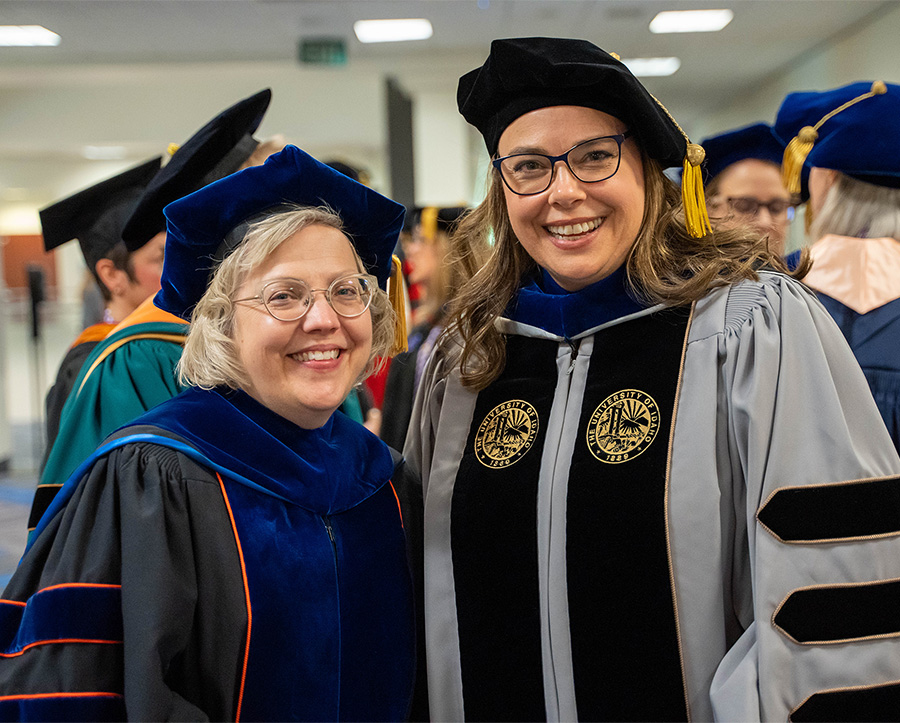 Close up of Spurlock and Poole wearing their doctoral regalia and smiling.