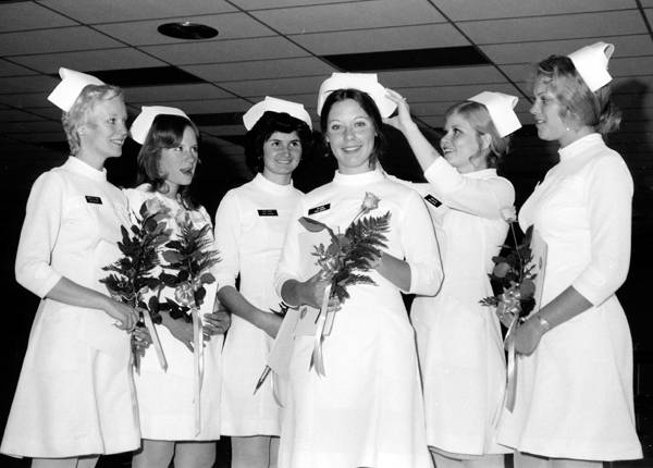 Black and white images of a group of nursing graduates holding flowers and wearing white caps.