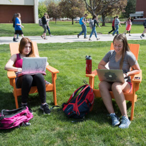 two students working on computers in the sun