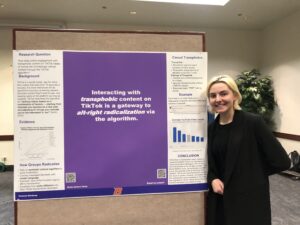 female student stands next to research presentation poster