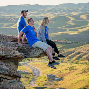 three Boise State students sitting on the edge of a cliff enjoying the view of green rolling hills and valleys