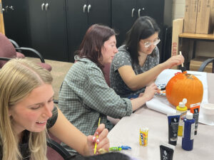 Group of students paint pumpkins sitting at a table on campus