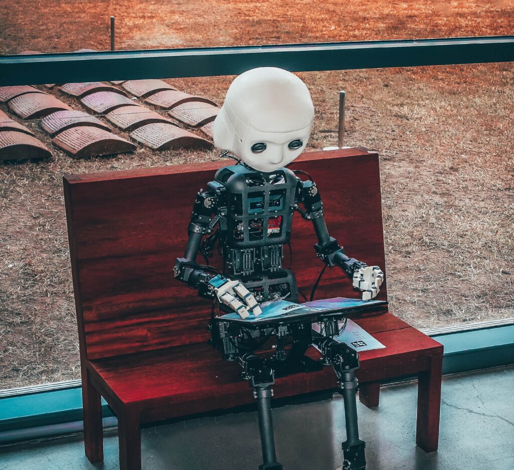 Child sized robot sitting on a small bench looking at a book