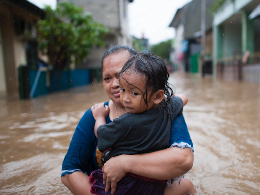 A woman holds a child in waist-deep floodwater.