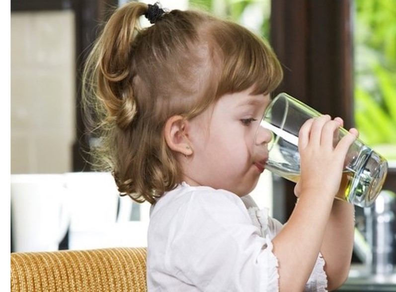 A toddler drinks water from a glass.